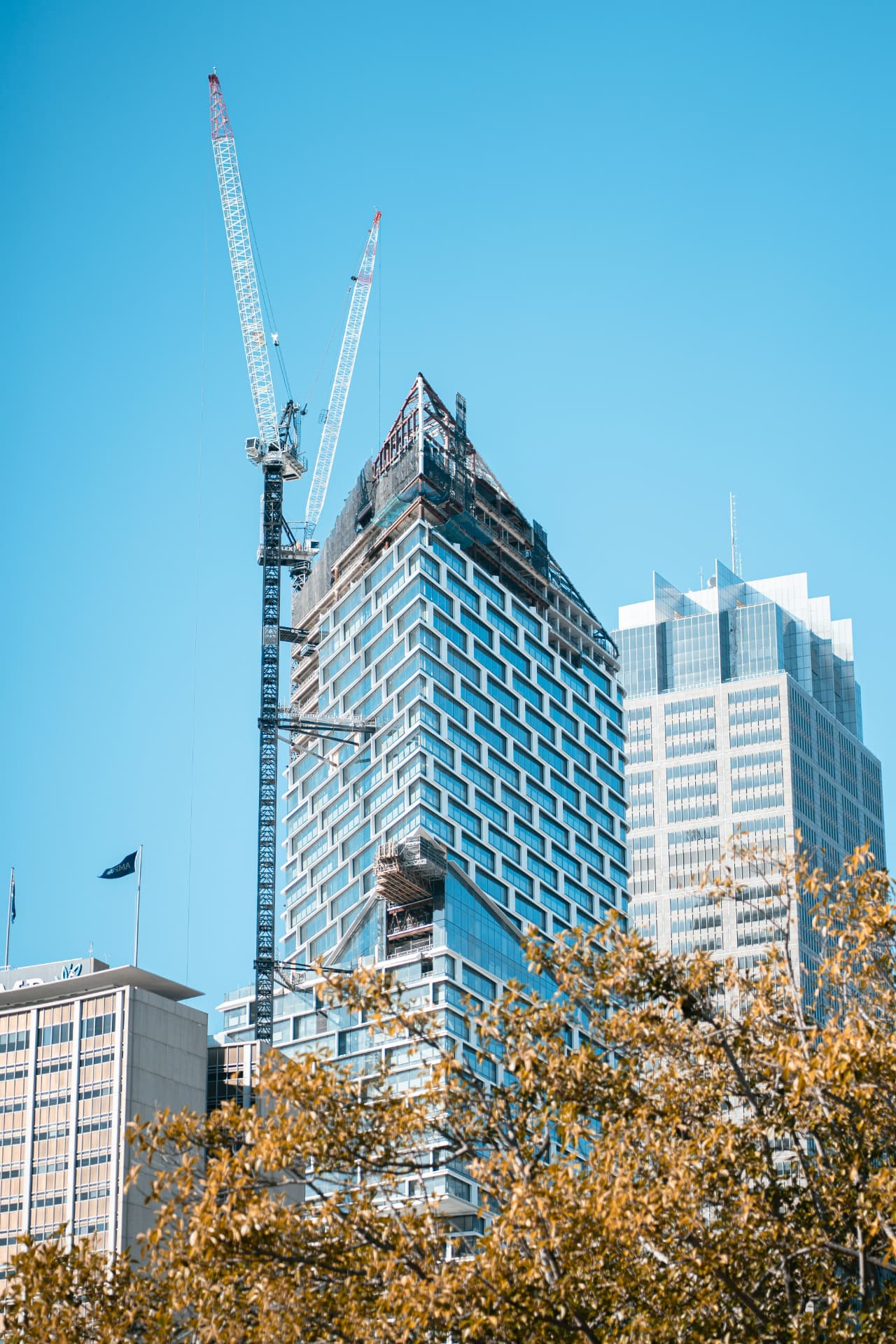 High-rise shell construction with two cranes against a clear blue sky. (AI-generated image)